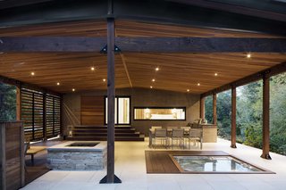 How to Refresh a Midcentury Gem in Quebec? Winter-White Everything - Photo 4 of 12 - The open terrace is fitted with recessed lighting by Foscarini and a StoneTile floor. It houses an outdoor kitchen and dining area, as well as a fireplace and a spa. Inside, it connects to a gym and sauna in the basement.