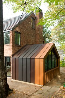 The den, originally and enclosed porch off the back of the house, was one of the biggest energy-sucking culprits. The designers opened it to the rest of the house to improve circulation, added a pentagonal Weather Shield window, and clad the structure in metal panels matching the roof. 