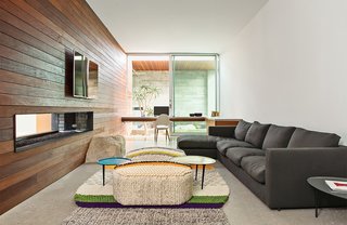 In the lounge, a sofa from Flexform joins a rug and poufs from Gandia Blasco. "We used boulders found onsite in the walls and windows as a way to reinforce the home's connection with the desert environment," Lockyer explains. As throughout, the wall and ceiling are painted with Cool December from Dunn-Edwards.