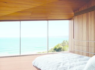 The couple, both surfers and beach lovers, wake up to stunning views of the azure-blue Southern Ocean in their otherwise monochromatic eucalyptus master bedroom. Wardle's firm designed the bed base, and the panel in the ceiling hides a television.