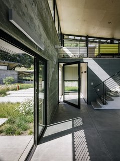 The entrance to the main pavilion is defined by a pivoting glass door from Fleetwood (above left). The stairs lead to the media loft, where Inga Sempé’s Ruché sofa for Ligne Roset breaks up the gray. Among the couple’s few directives were tall ceilings, which Feldman covered in low-cost plywood sheets.