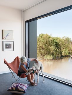 With a large glass door from Capral that opens completely to the elements, the master bedroom becomes part of the landscape. Imogen sits with Millie, one of the family’s two greyhounds. The art is by Noel McKenna (top) and Ray Crooke; the butterfly chair cover was custom-made by a saddler. The carpet is from Supertuft. 