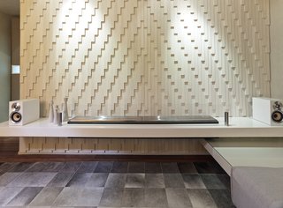 Inspired by a dress made out of razor clam shells by the late fashion designer Alexander McQueen, the designers created a custom wall with individually laid pieces of Island Stone tile. It accents a minimalist EcoSmart fireplace. 