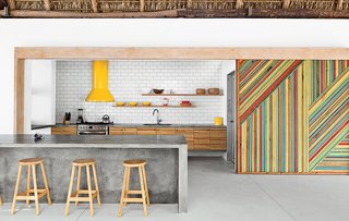 Bursts of Yellow and Indoor Gardens Are Just Two Reasons to Love This Home - Photo 2 of 5 - By eliminating walls and incorporating a series of interior gardens, architect José Roberto Paredes creates an eclectic and inspired El Salvador beach house. In the kitchen, rough-hewn materials like a eucalyptus-log-and-thatch roof offset the monolithic concrete island and glossy subway tile backsplash. Claudia & Harry Washington built the vivid wooden sliding walls, which are inspired by the palm leaves that change color and create diagonal patterns in trees near the house. The bar stools were a street market discovery.