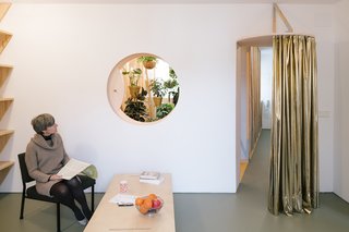 A cutout oculus in the living room offers a peek into the plant-filled bath, while a curtain can be drawn to control airflow.