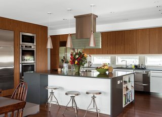 Inspired Indoor Teak Looks - Photo 8 of 14 - In the kitchen, teak-and- thermofoil cabinets and Caesarstone countertops mix with Miele appliances—wall ovens, induction cooktop, hood, and microwave—and a Sub-Zero refrigerator. The kitchen sink and faucet are by Blanco. The owners, who split their time between Fishers Island and Great Britain, found the vintage pendant lamps at Lassco architectural salvage.