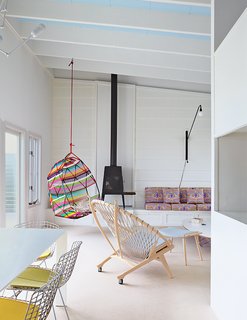 How a Smart Interior Design Saved This House - Photo 4 of 9 - Alexandra Angle transformed a beachside cabin into a colorful retreat for a college friend and her family. The living area features a PP130 Circle Chair by Hans Wegner and a Shaker wood stove by Antonio Citterio with Toan Nguyen for Wittus. A Tropicalia Cocoon hanging chair by Patricia Urquiola complements the fabric from Liberty that Angle used for the cushions on the built-in banquette. 