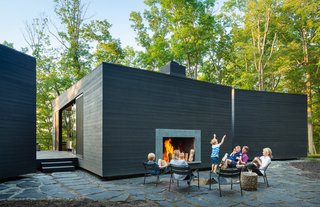 Unlike the north-facing side of the home, the south-facing facade is completely windowless and opaque, with the exception of an outdoor hearth built directly into its side. The lounge chairs are from IKEA, and the MacNellys sourced the slate flagstones and gravel surrounding the home from a local quarry.