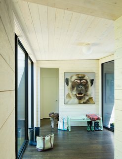 ARCHITECTUREFIRM used rough-sawn cedar paneling throughout, cladding the exterior with blackened pieces, and whitewashing the interior surfaces to form a dramatic visual contrast between inside and out. A painting by artist Tim Harriss hangs above a Crane bench by Double Butter near the entry hall