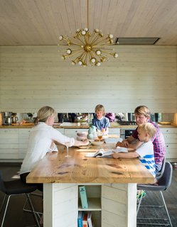 The kitchen island, designed by ARCHITECTUREFIRM and custom-fabricated with pine by Peter Johnson Builders, doubles as a dining table. It's paired with Inmod barstools, and a brass-and-crystal Sputnik chandelier by Jonathan Adler, which hangs overhead.