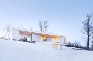 Squinting through Quebec's seasonal fluries, one might not immediately register the Nook Residence, an all-white retreat that purposefully blends into the winter landscape. The house, designed by MU Architecture, presents itself to passersby as a blank monolith; yet around the corner, it opens onto Lake Memphremagog through expansive windows and an interior balcony. 