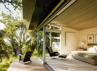 Sloped ceilings, covered with stained Western red cedar, add warmth to the interior (bottom). "We set out to design using the best of what modernism has to offer, but to try to execute that in a way that is livable and home-like," says architect Jonathan Feldman. The bedroom contains an A. Rudin bed and a Beau chair from Room & Board. It opens onto a deck with an aluminum awning.