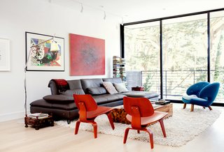 The main floor is arranged as one long, contiguous space, with a living area and balcony at the front end. An Aulia coffee table by Henk Vos, a pair of red Eames molded plywood chairs, and a Pelican chair by Finn Juhl center the space.