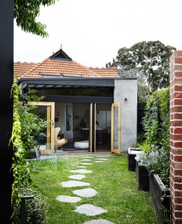  On the back facade, cement render and black-painted steel update the existing terra-cotta roof tiles. Custom glass doors fabricated by TCM Building Group open onto the garden, where a stone path leads to a new building housing Kate’s studio and Tom’s wine cellar.