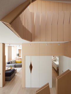 What’s the Twist Behind This Home’s Sinuous Staircase? Ordinary Plywood - Photo 6 of 14 - Tehrani designed the millwork throughout, collaboratingwith fabricator C. W. Keller + Associates. Seen from the foot of the central staircase, a set of blue, gray, and yellow Alphabet sofas by Piero Lissoni for Fritz Hansen furnish the family room on the first floor; the dining area lies just beyond, adjacent to the kitchen. A small aperture provides a peek into the second stairwell, which is situated at the center of the floor plan and leads to the garden level.
