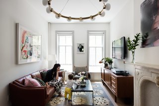 Modern Becomes Eclectic in This Renovated Brooklyn Townhouse - Photo 1 of 13 - Interior designer Merrill Lyons plays with her son in the Brooklyn home she renovated with her husband, Charles Brill, a lighting designer and cofounder of New York–based company Rich Brilliant Willing (RBW). The couple’s design sensibility is marked by a warm mix of historic periods and styles, punctuated with pieces by RBW, including the circular brass Cinema chandelier that hangs in the living room. The leather sofa and teak credenza are vintage; the 1960s rosewood Genius armchair by Danish designer Illum Wikkelso was reupholstered with fabric sourced from an outlet.
