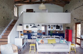 Over a Decade, Two Furniture Designers Reimagine a 300-Year-Old Barn - Photo 2 of 11 - Paired with a lime rendered staircase, a gray Moreau sofa by Pinch and vintage yellow side tables offer bright contrast to the living room’s limestone walls and timber frame. The couple laid some 20,000 pieces of reclaimed oak to create the floor’s herringbone pattern.