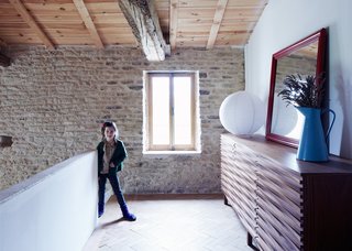 Over a Decade, Two Furniture Designers Reimagine a 300-Year-Old Barn - Photo 7 of 11 - Floris, seven, stands on the mezzanine next to a walnut version of the Wave sideboard her father designed for Content by Terence Conran. The enamel water jug was found at a local brocante market.