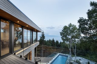 The second floor includes another open plan that blends the kitchen, dining area, and living room together. After ascending to the top, another deck folds over the pool to create an overhang. The wide-spanning glass wraps around the top of the cantilever to take full advantage of the natural setting. 