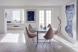 The first floor of the home features an open plan that combines the kitchen, dining room, and a small study. Drop chairs by Arne Jacobsen surround a PK58 table by Poul Kjærholm. The study includes the designer's three-legged PK11 chair alongside sculptures by artists and the couple's children. 