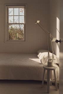 The all-white guest bedroom features a West Elm bed, covers by Garnet Hill, and a Tizio desk lamp by Richard Sapper for Artemide