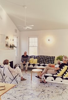 Residents Ann and Tony Spagnola sit with their architects, Peter Stamberg and Paul Aferiat, in front of the whitewashed brick fireplace in the living room. A vintage Butterfly chair joins custom sofas designed by the architects. Coffee tables by Alvar Aalto for Artek and pillows by Marimekko create a clean, Finnish-inflected environment.