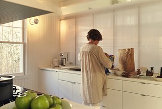 .In the galley-style kitchen, Ann sorts groceries into Akurum cabinets from IKEA. For the sconces, the architects selected generic porcelain sockets, then stylized them with silver-cap bulbs. 