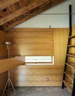 A custom ladder made of bent steel with oak treads leads to the sleeping loft, while a white oak panel swings opens to reveal an inset window. Longtime collaborator Jeffrey Kramer crafted the home’s wood elements. 