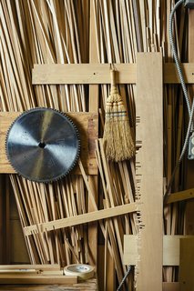 The saw blade, whisk broom, and aligning board that the craftsmen use to create screens hang on a shop wall. 