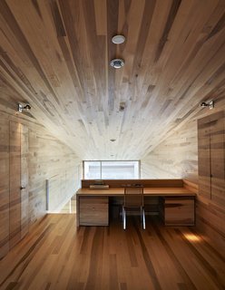 The poplar desk at the end of the master bedroom loft looks down on the living areas beneath the slanted, wood-clad ceiling. The compact interior of the house was inspired by ship-building techniques, with built-in furniture and storage throughout.