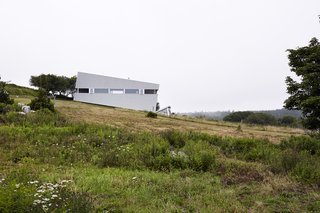 Imagined as a jewel box on a hill, Sliding House takes the place of a barn that once stood on this Nova Scotia site. Its form follows the slope of the land, while the windows are parallel with the horizon, setting up a tension between a plumb interior and a slanted exterior. The tilt of the structure isn’t just a visual trick—it also helps the roof to drain. When the distinctive windows are lit from within, the house serves as a beacon for local sailors. 