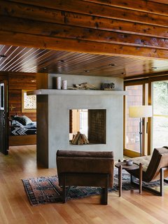 An Eclectic Pacific Northwest Cottage - Photo 2 of 13 - Bruce Livingstone’s seaside getaway in British Columbia features a remarkably open layout. The master bedroom flows into the living room, where Griffin lounge chairs by Lawson-Fenning face a fireplace clad in glass fiber–reinforced concrete panels by Wiersma Masonry. 
