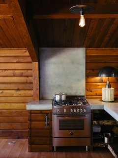 An Eclectic Pacific Northwest Cottage - Photo 5 of 13 - A Column lamp by Apparatus and concrete countertops join a Bertazzoni propane range. The brass pendant<br>is by Workstead.