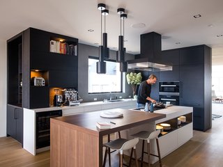 The black steel A110 pendants by Alvar Aalto match the Poliform ventilation hood and ebonized white oak cabinets by Leicht Haus. LED lighting is integrated into the island shelving. The drawers underneath are handleless and open electronically by touch using a servo drive. 