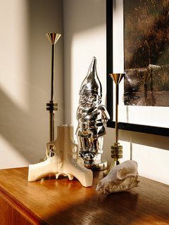 A pair of Tom Dixon Cog candle holders and a 3Guns vase by Suck UK are assembled atop a vintage teak sideboard. 