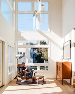 Tom and Kate own the top two floors of the building. On the lower level, in the double-height foyer, Milo Baughman's Recliner 74 is positioned beneath Rudi Double Loop pendants by Lukas Peet for Roll & Hill. The floor lamp is a custom piece that De Angelis Designs adapted from a vintage salon hood dryer. The staircase follows the bedroom's new primary material, French white oak. 