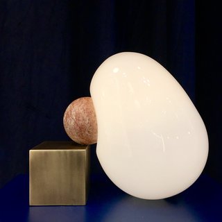 The Dimple Light by Anna Karlin is a blown-glass form into which a metal sphere is fused, creating a divot or a dimple in the shape. It adjoins a complementary brass cube. 