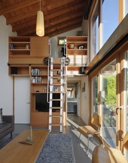 The double-height interior features an upper loft accessed by a custom wood-and-aluminum rolling ladder. 