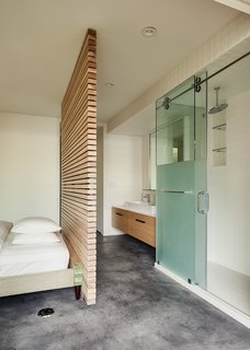 The motif of slatted hickory continues in the bold open-plan master suite, which features multifaceted Diamond White tile by Porcelanosa and a Hoffman bed, with its headboard removed, from Room & Board. 