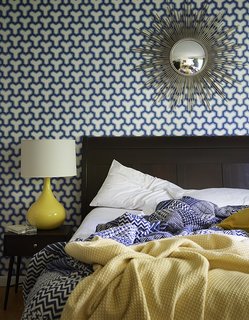 A sunburst mirror, which George bought on eBay, pops against patterned Antonina Vella wallpaper in the guest bedroom. The lamp is vintage. 