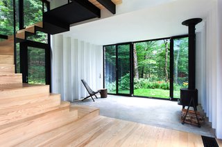 Growing Upward and Outward, a Cabin Expansion Mirrors the Trees - Photo 4 of 10 - The addition rises above the original shack's 400-square-foot concrete foundation, which is partially visible in the living room. A Cricket patio chair by Hershy Way is used for indoor seating opposite a Morsø wood-burning stove. 