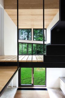 Growing Upward and Outward, a Cabin Expansion Mirrors the Trees - Photo 6 of 10 - The second floor is a master bedroom, bathroom, and mechanical room, along with an open volume that fills the house with light from the Alumilex doors and windows. The paint is Distant Gray by Benjamin Moore. 