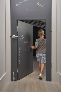 In certain places, the scale of the home is adjusted for children. A standard door, covered in chalk-board paint, has a 48-inch-tall door set inside it. 