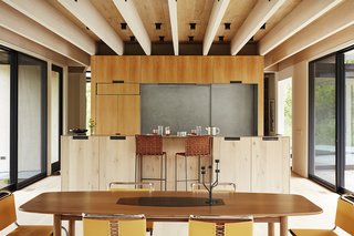 In the kitchen, bar chairs by Mark Albrecht Studio complement the white-oak cabinetry and stainless steel countertops fabricated by D. Reis Furniture. 