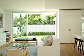 The living room is defined by large glass sliders by Fleetwood that open up to the backyard, allowing light to flood the downstairs space. The room features a Crosby sofa by West Elm, CH25 lounge chairs by Hans J. Wegner for Carl Hansen & Søn, and an OW 150 daybed by Ole Wanscher. 