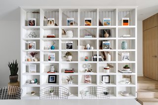 The large built-in shelving unit acts as a multifunctional divider between the dining space and the staircase.