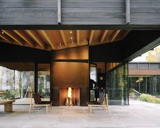 Plagued Ash Trees Were Repurposed to Create This Charred-Cedar Clad Home on Lake Michigan - Photo 4 of 9 - The home’s undulating roof, composed of exposed wood beams and plywood sheathing, references the rolling terrain. A Cor-Ten steel–clad outdoor fireplace was built by BRD Construction; the same material was used for the interior fireplace, as surround on some windows, as cladding for the garage door, and on the chimney. The lounge chairs are from the Finn Collection from Design Within Reach. Tim Kirby of Surface Design Inc. tackled <br>the site’s landscape architecture.