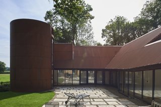Corrugated sheets of weathered steel form the walls and roof of the extension, while the two-story tower is clad in smooth, curved panels. The rusty material contrasts beautifully with the home's verdant surroundings. 
