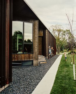 Beyond a bed of black granite rocks, an entrance is concealed in an alcove in the home’s cedar-and-weathered-steel facade. The windows were manufactured by Duxton Windows & Doors. 
