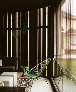A veil of Cor-Ten steel and a motorized blind from Phantom Screens filter sunlight on the screened porch. The Acapulco chair and Sonny Hanging planters are from CB2.